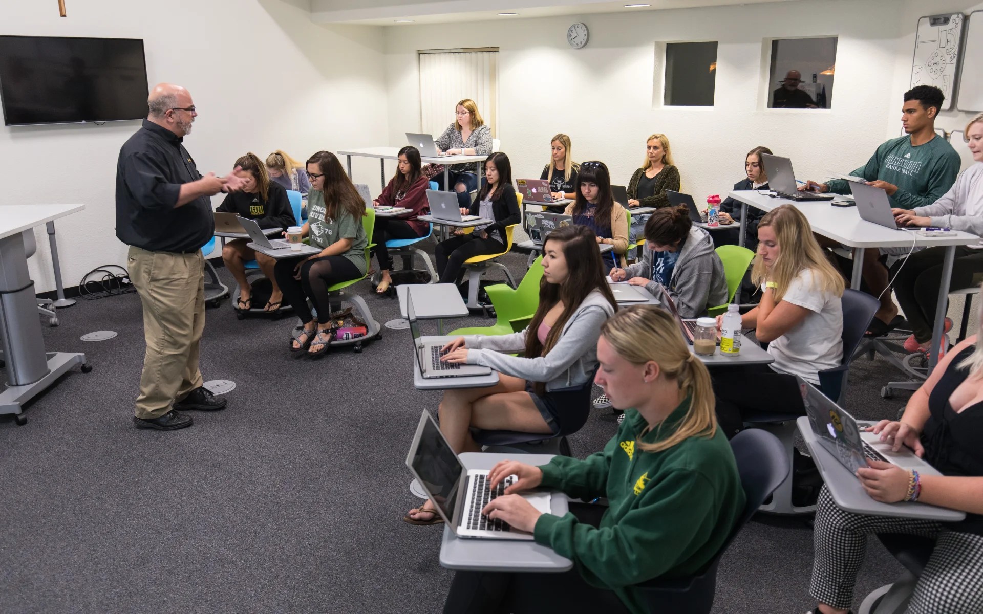 Professor teaching a college class with students using laptops in a modern interactive classroom