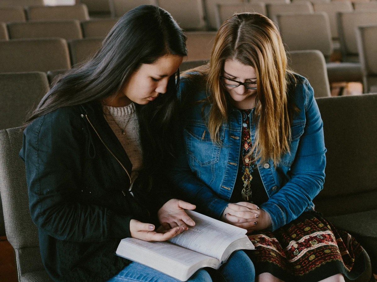 Two women sitting on a bench looking at a book