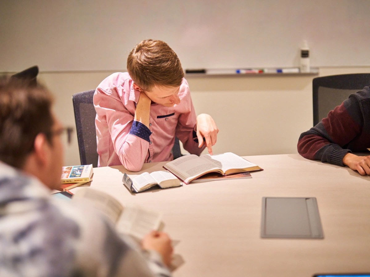 A group of people sitting at a table reading a book