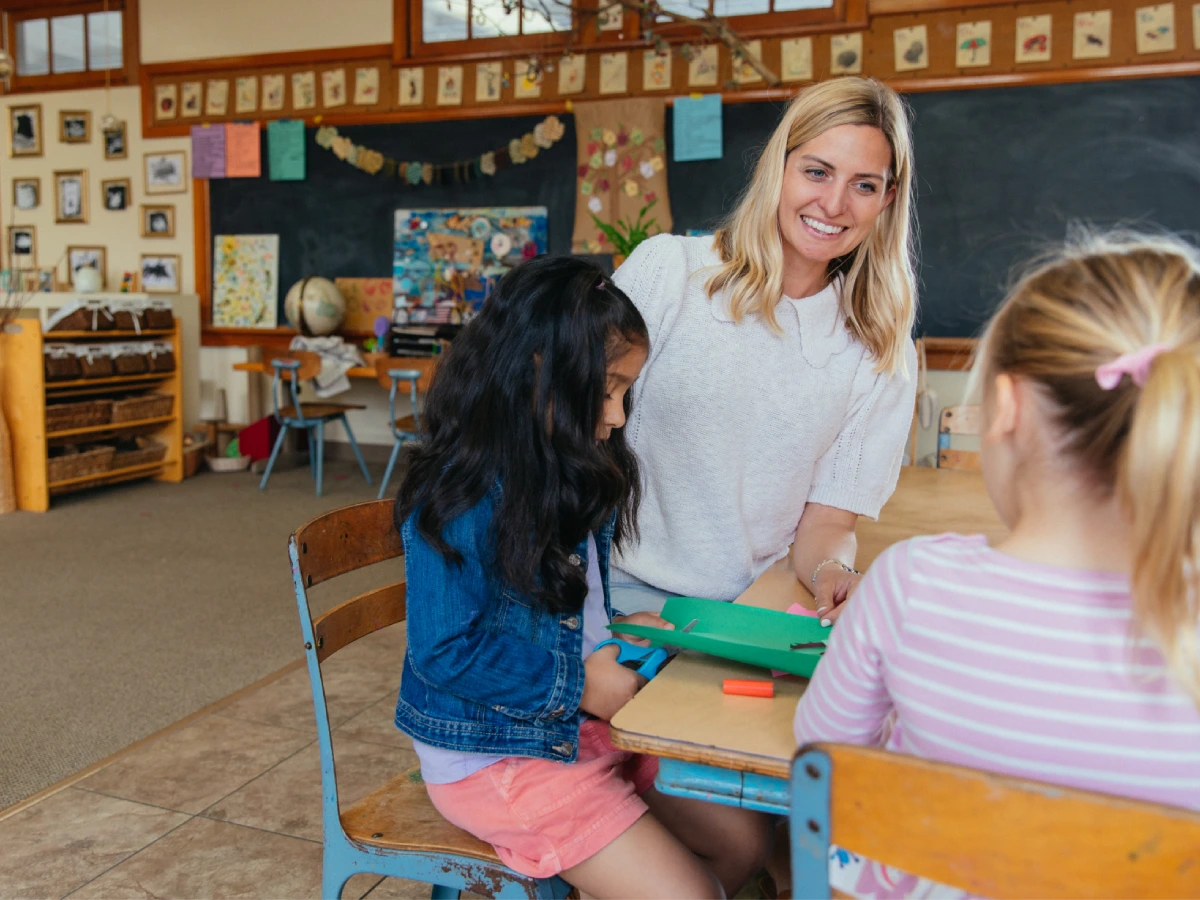 A woman and two girls sitting at a desk in a classroom