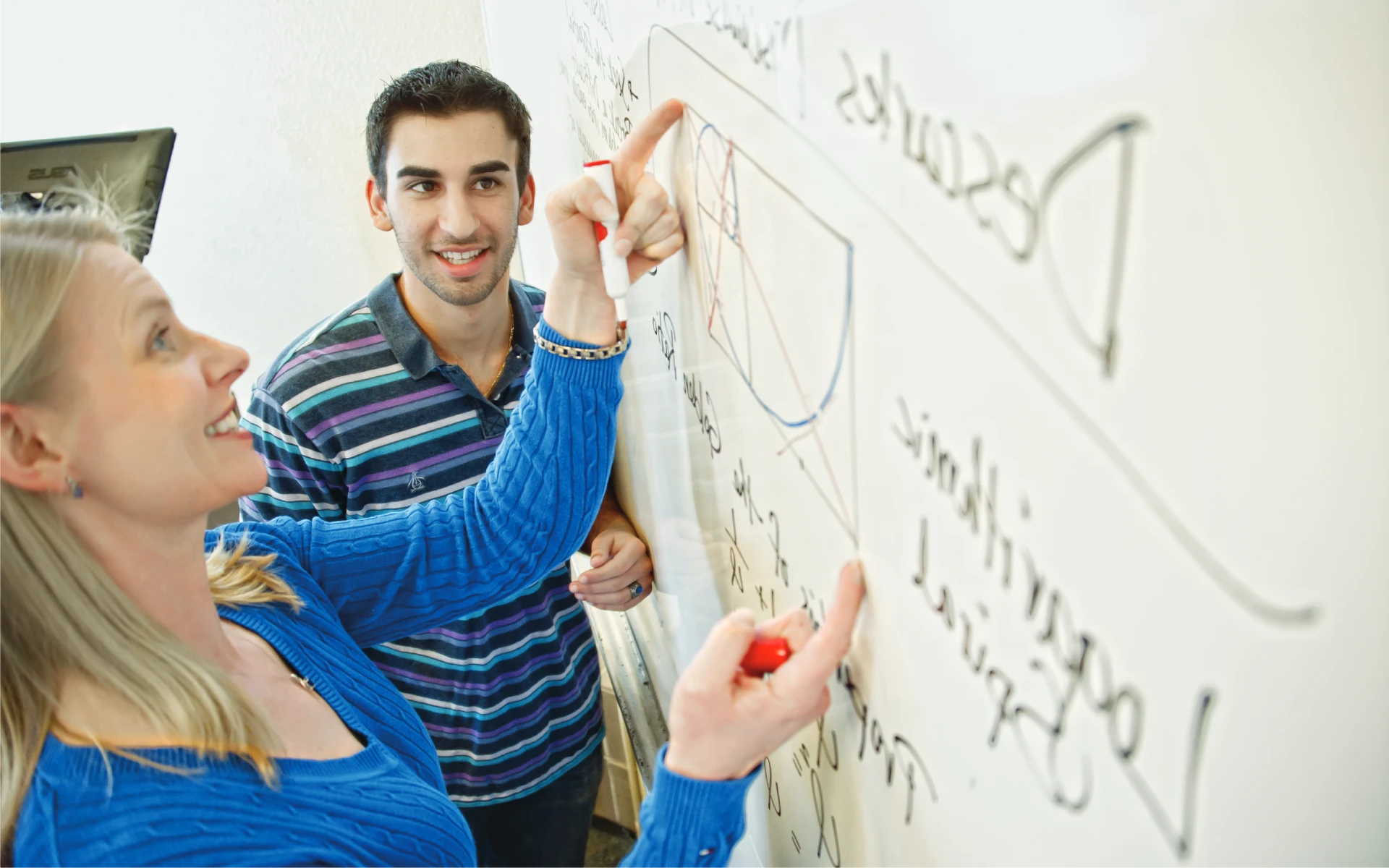 A faculty member and student discuss a diagram drawn on a whiteboard, collaborating during class