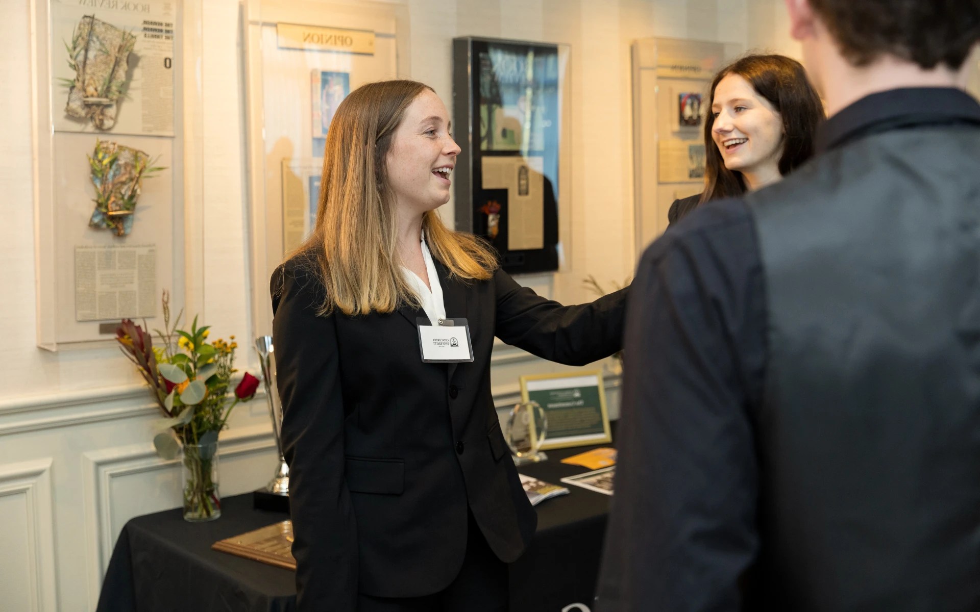 A student in business attire smiles and shakes hands during a networking event at Concordia University Irvine