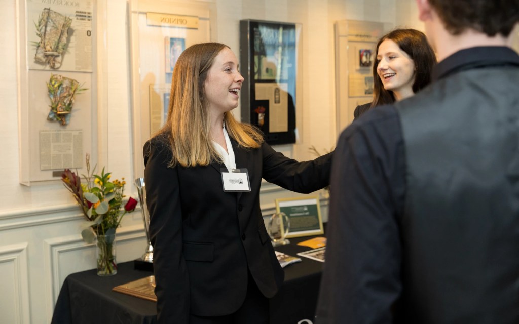 A student in business attire smiles and shakes hands during a networking event at Concordia University Irvine