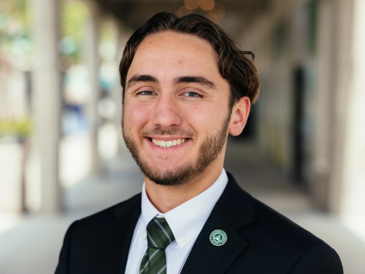 A student in formal business attire smiles confidently while wearing a green striped tie and suit jacket with a Concordia University Irvine pin