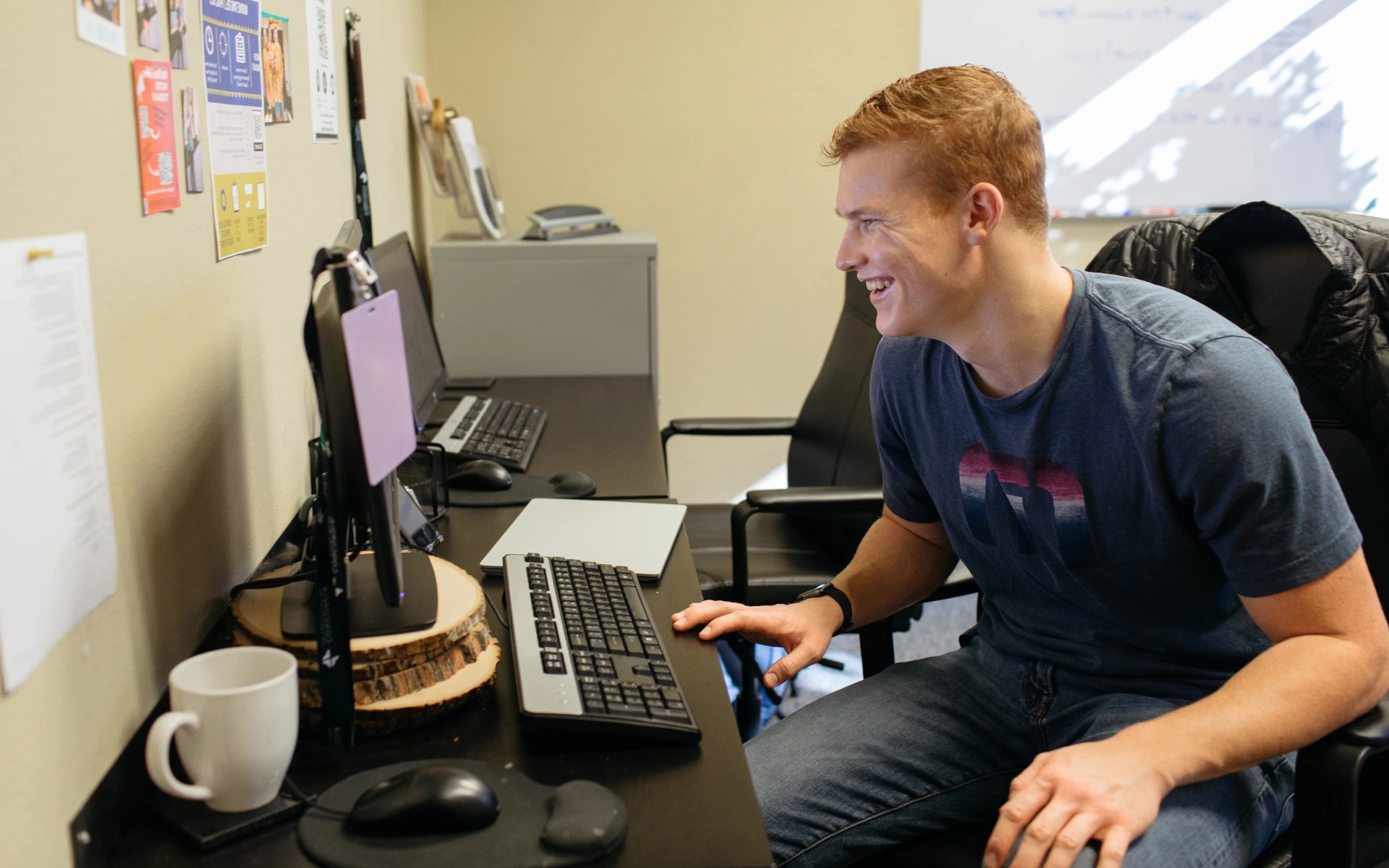 Person sitting at a desk smiling while working on a computer in an office environment