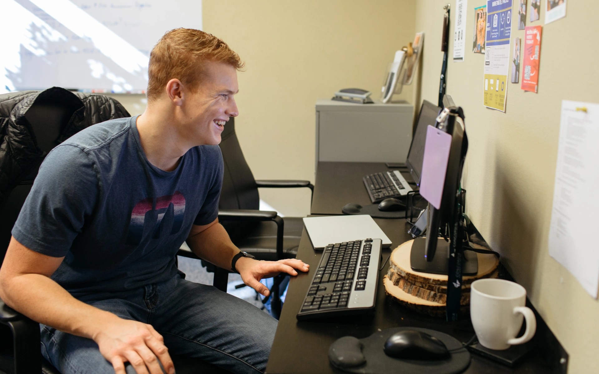 Person sitting at a desk smiling while working on a computer in an office environment