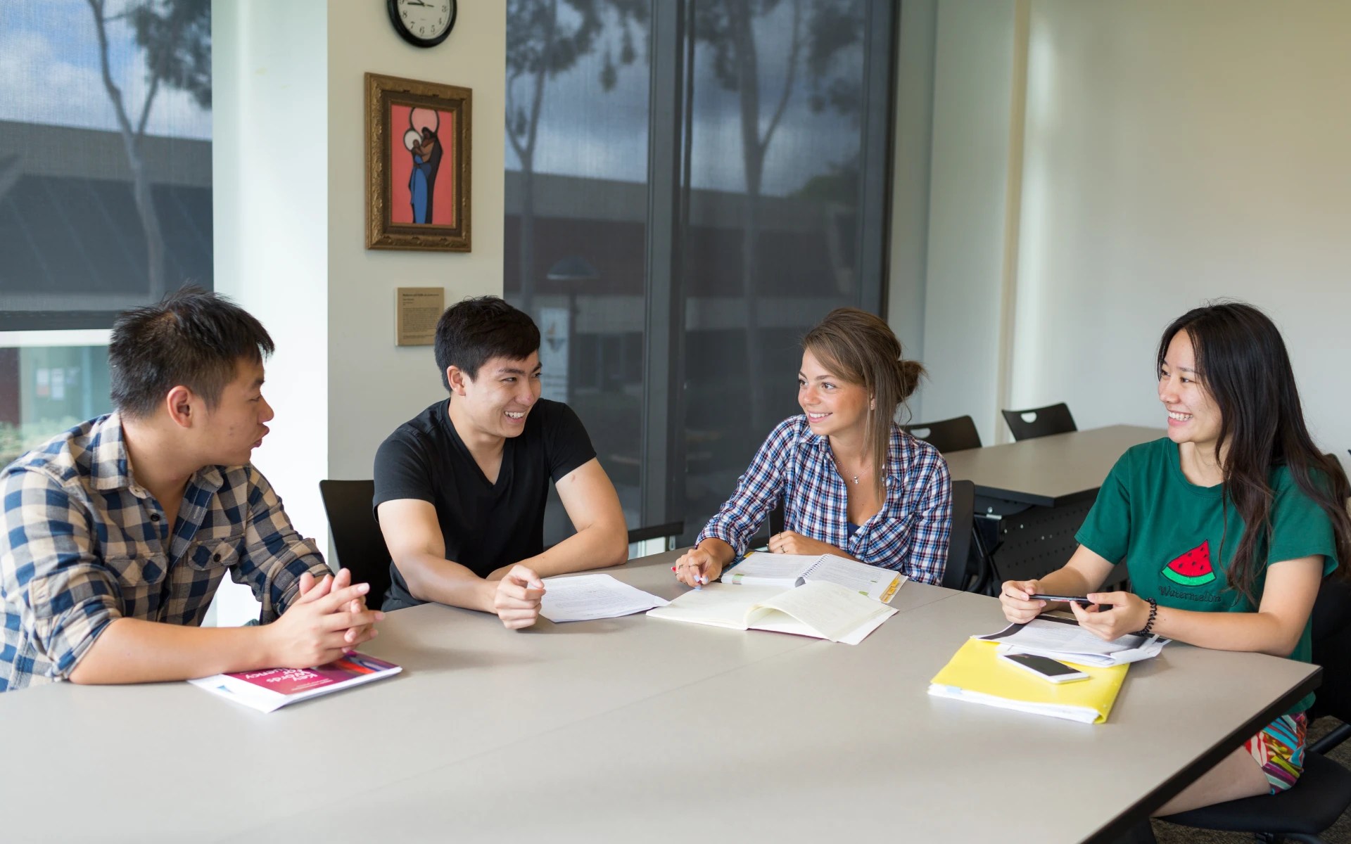 Four students sitting around a table in a classroom working together on an assignment and smiling