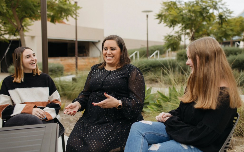 Three students sitting outside on campus, smiling and talking together