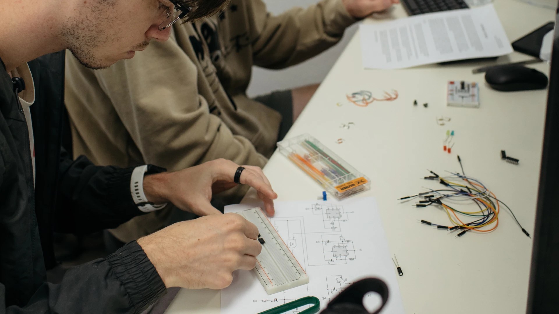 Two students working together on an electronics circuit project using a breadboard and computer