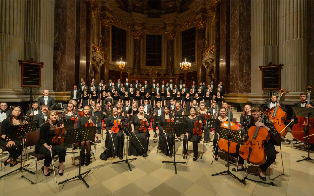 A university choir and orchestra performing in a grand cathedral with musicians and vocalists dressed in formal concert attire