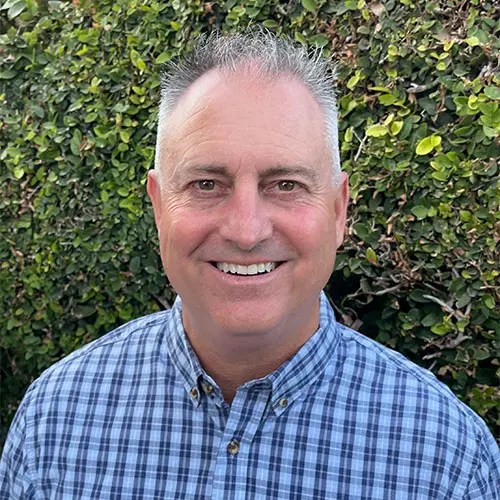 A man smiling in front of a bush