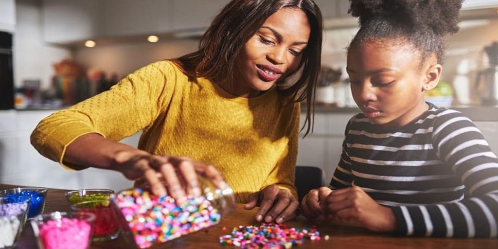 A woman and a child looking at a jar of colorful beads