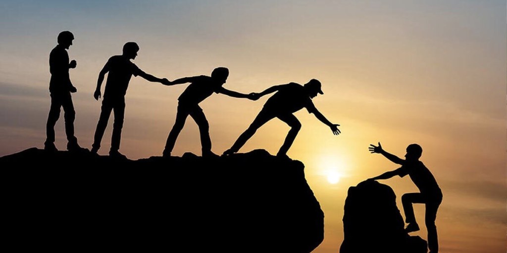 Silhouette of people helping each other to reach the top of a cliff