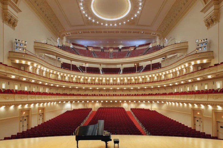 A piano in a concert hall with Carnegie Hall in the background