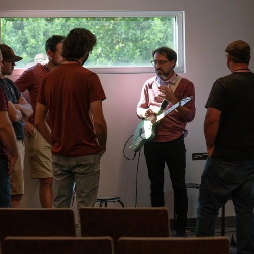 A man playing a guitar in a room with other people