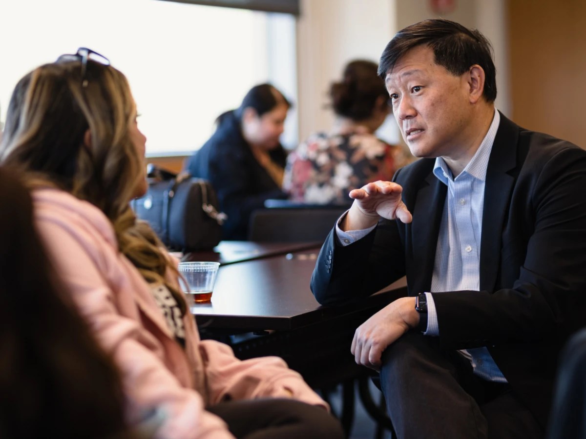 A man in a suit sitting at a table with a woman in the background