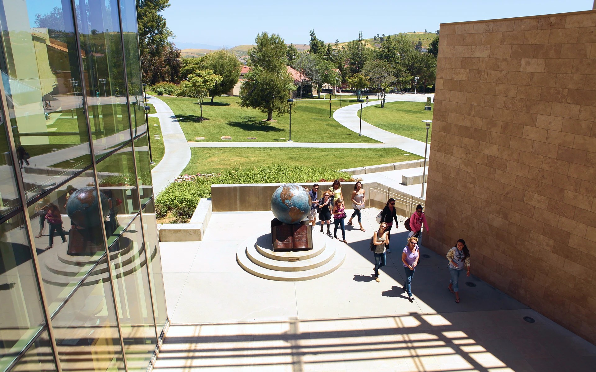 A group of people walking around a globe statue