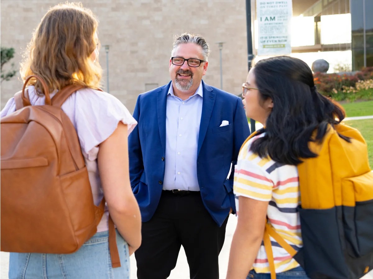A man in a suit and glasses talking to a group of people