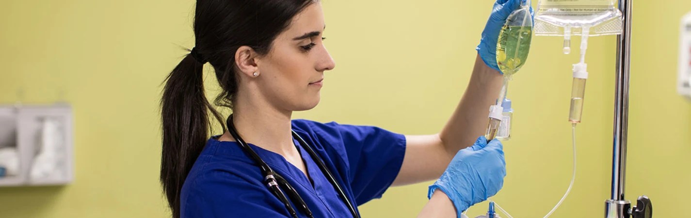 A woman wearing blue scrubs and stethoscope holding a syringe