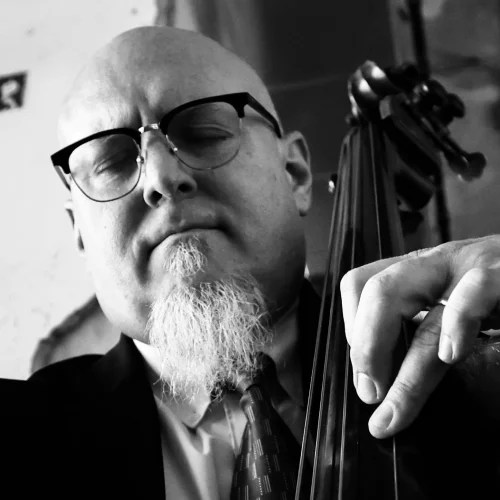 A man with a beard and glasses playing a cello