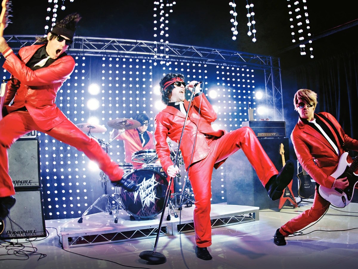 A group of men in red leather on stage with microphones and lights