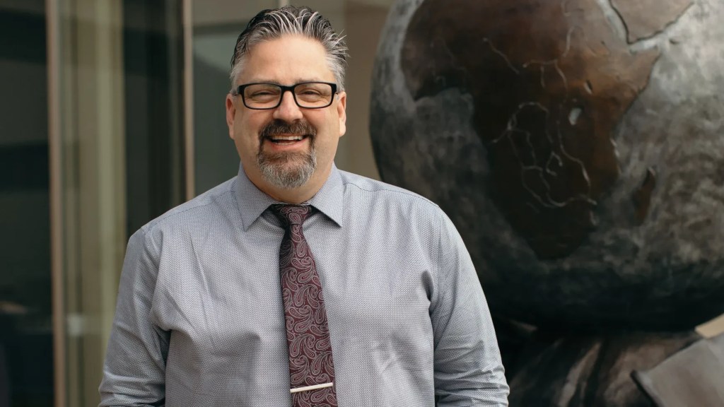 A man smiling in front of a statue