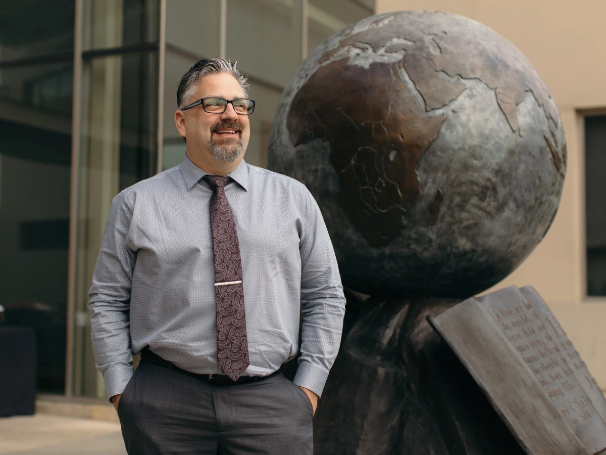 A man in a tie and glasses standing in front of a statue