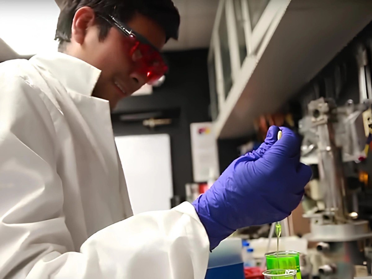A man in a lab coat and gloves holding a dropper