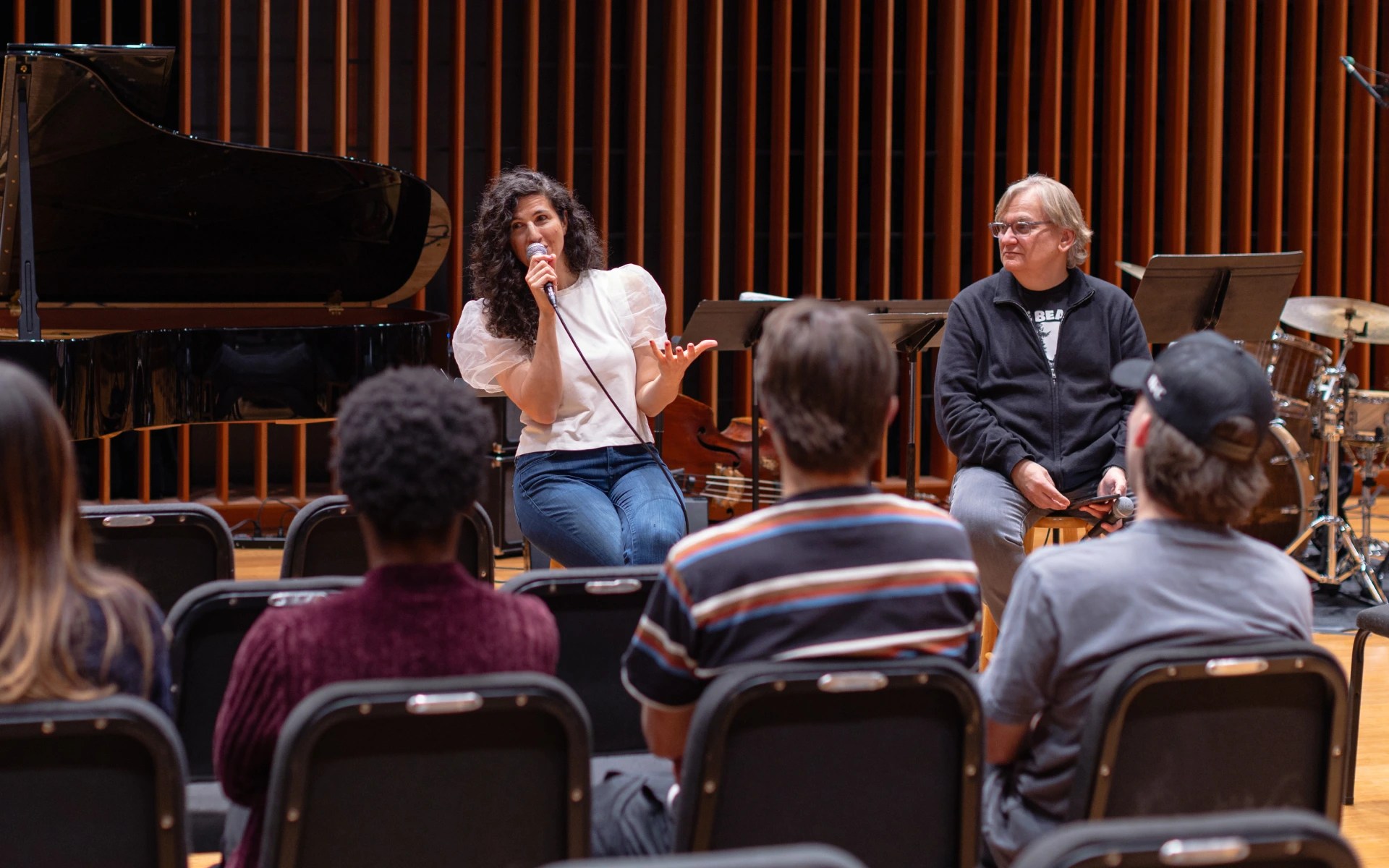 A woman singing into a microphone with a group of people sitting in chairs