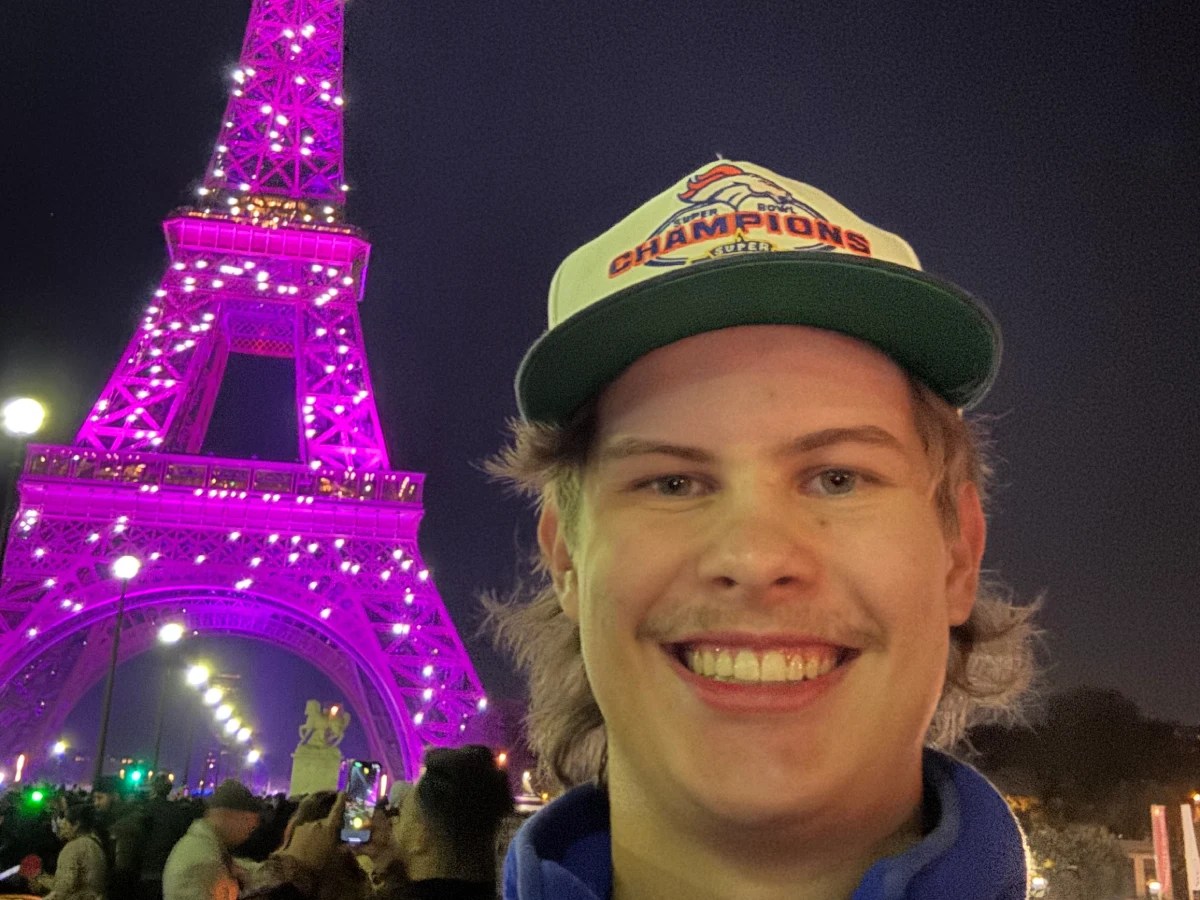 A man taking a selfie in front of a pink lit tower