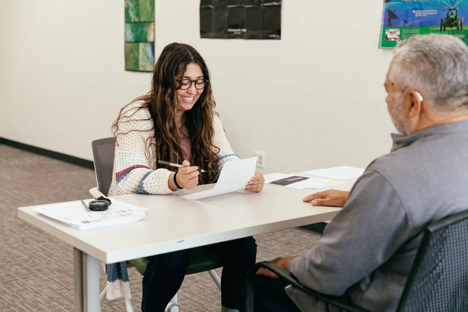 A student research assistant smiles while completing a survey with a participant at a table.