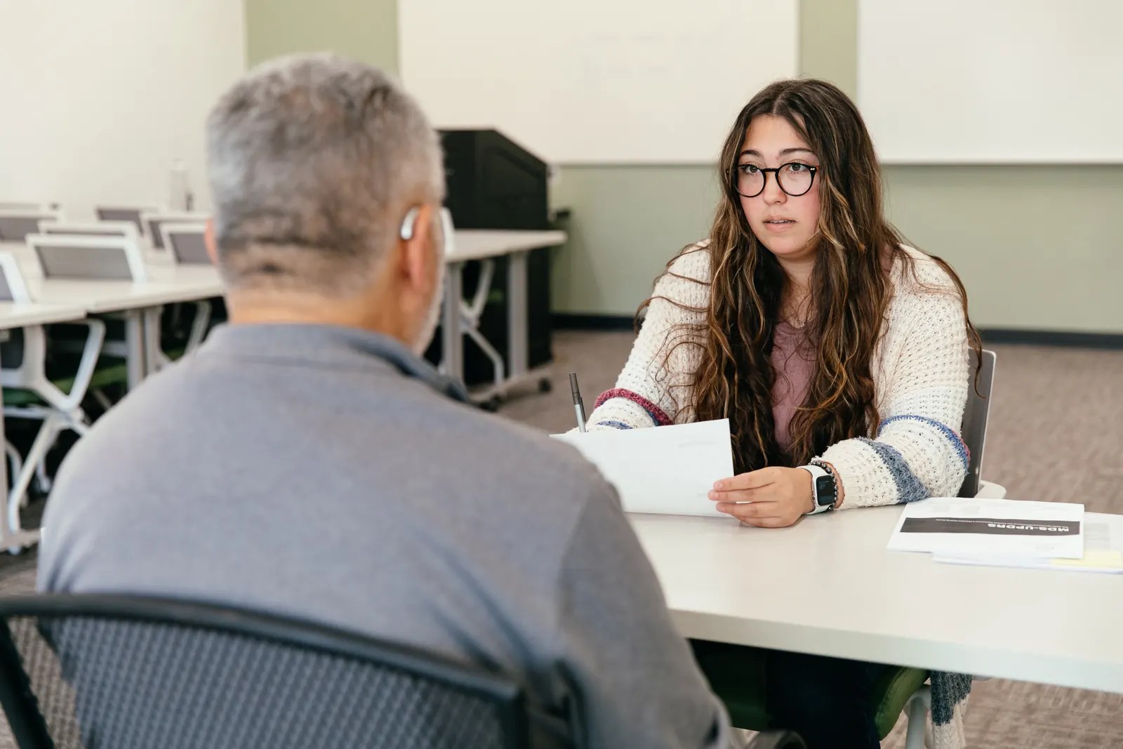 A student research assistant interviews a participant at a table.