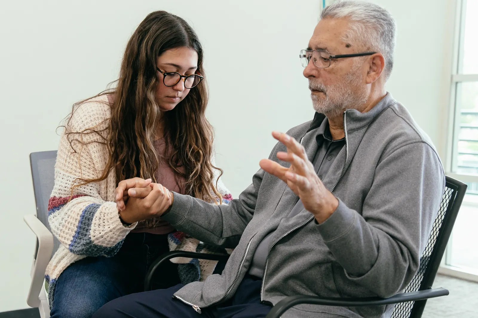 A student research assistant holds a participant's hand while he demonstrates a hand movement.