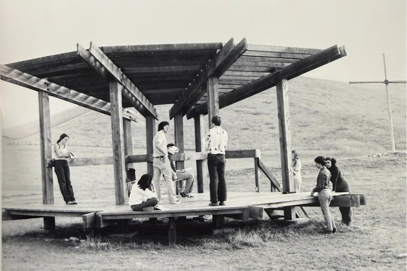 Black and white photo of students on and around the Bird Sanctuary, a wooden stage with an open roof frame.