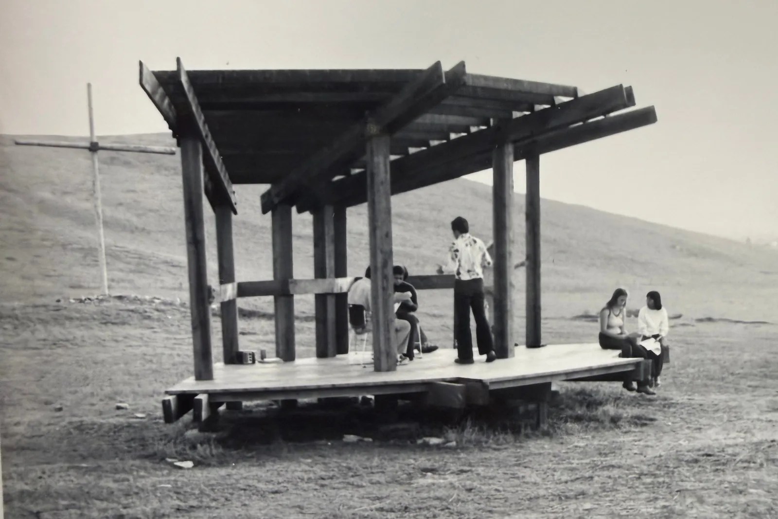 Black and white photo of students on the Bird Sanctuary stage, with a cross on the hill behind it.
