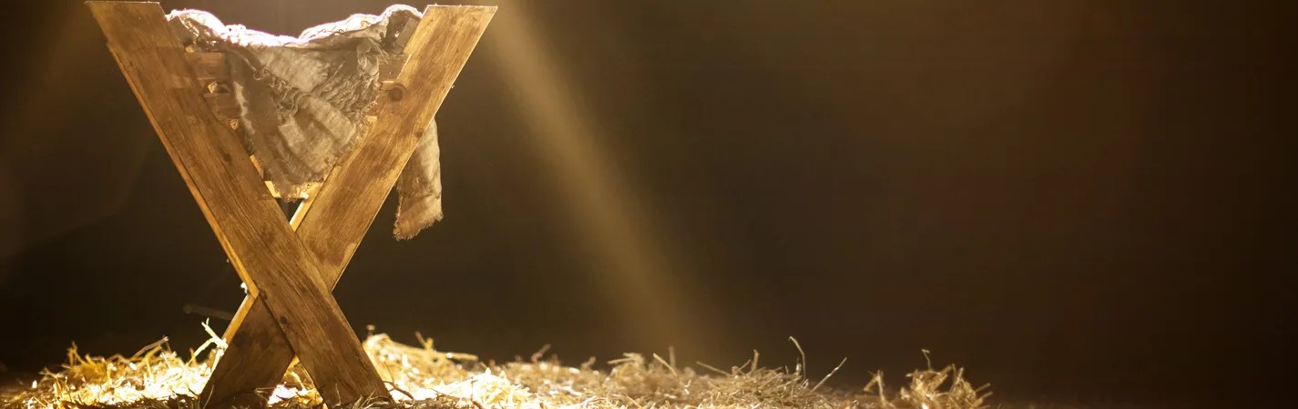 An empty wooden manger on straw, lit by a beam of light