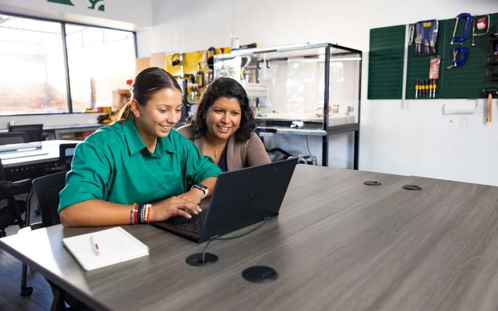 Two people smiling while working together on a laptop in a technology lab